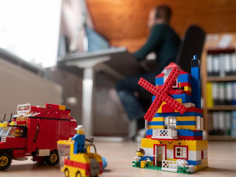 Ein Mann arbeitet im Homeoffice, während im Vordergrund Spielzeug seiner Kinder steht.