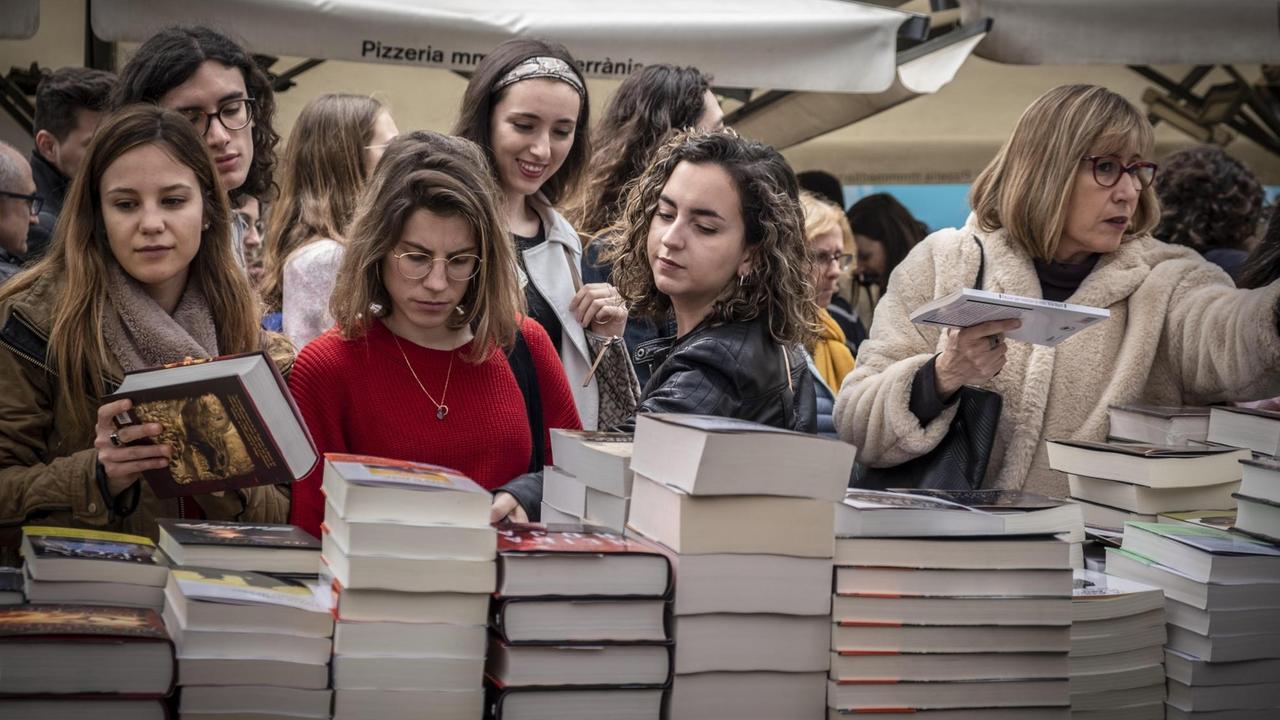 Junge Frauen stehen am Bücherstand und begehen den St. Jordan Tag in Barcelona.