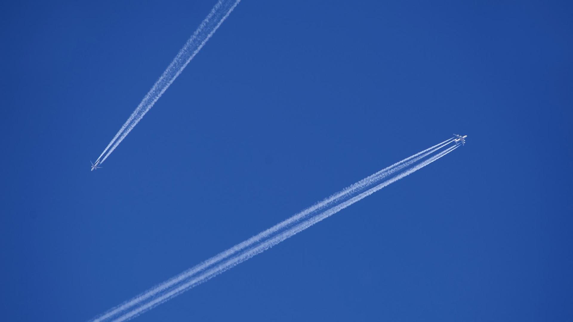 Zwei Flugzeuge mit Kondensstreifen am blauen Himmel.