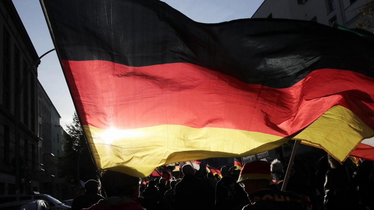 Teilnehmer der rechtspopulistischen Demonstration "Tag der Nation" des Bündnisses "Wir für Deutschland" ziehen am 03.10.2018 mit Deutschlandfahnen durch Berlin. Im Vordergrund eine große Deutschlandfahne, die Demonstranten im Gegenlicht.