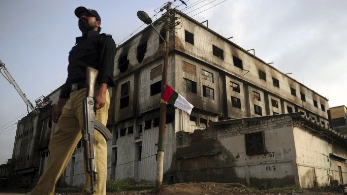 Ein pakistanischer Polizist steht vor der ausgebrannten Textilfabrik in Karachi, in der bei einem Feuer im September 2012 fast 290 Menschen ums Leben kamen.