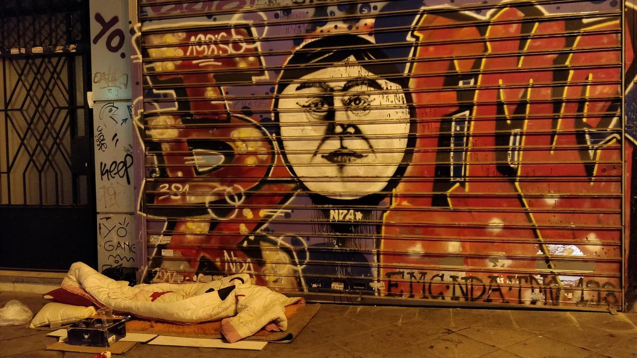 Ein Obdachloser liegt vor einer Wand mit Graffiti.