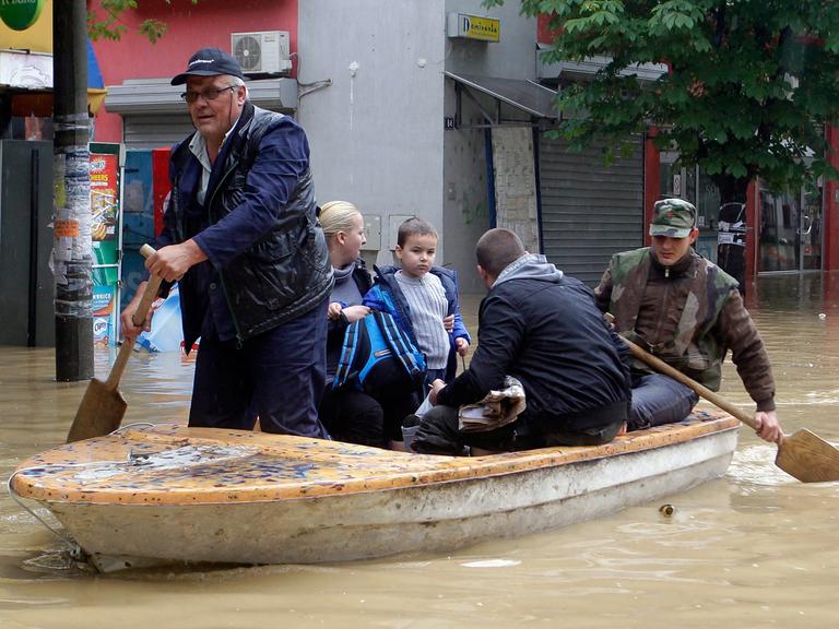 Ein Ruderboot mit Menschen fährt durch eine überschwemmte Straße in Obrenovac, Serbien