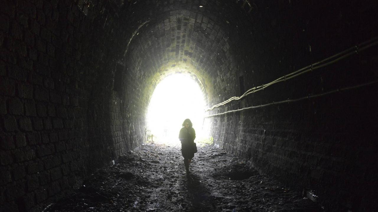 Ein Frau geht im Licht am Ende des Tunnels.