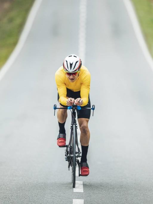 Ein Mann mit gelbem Shirt und Fahrradhelm fährt auf einer asphaltierten Strasse Rennrad