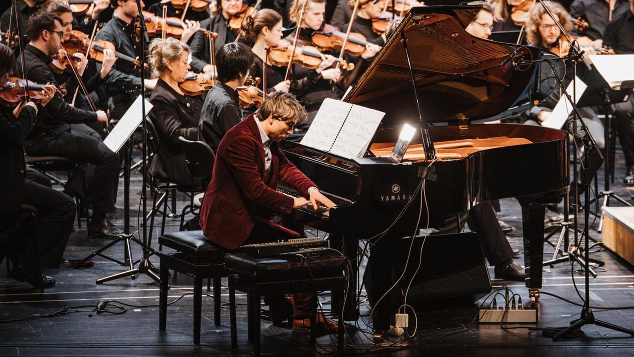 Der Pianist sitzt an einem Konzertflügel, an dem ein Synthesizer angeschlossen ist. 