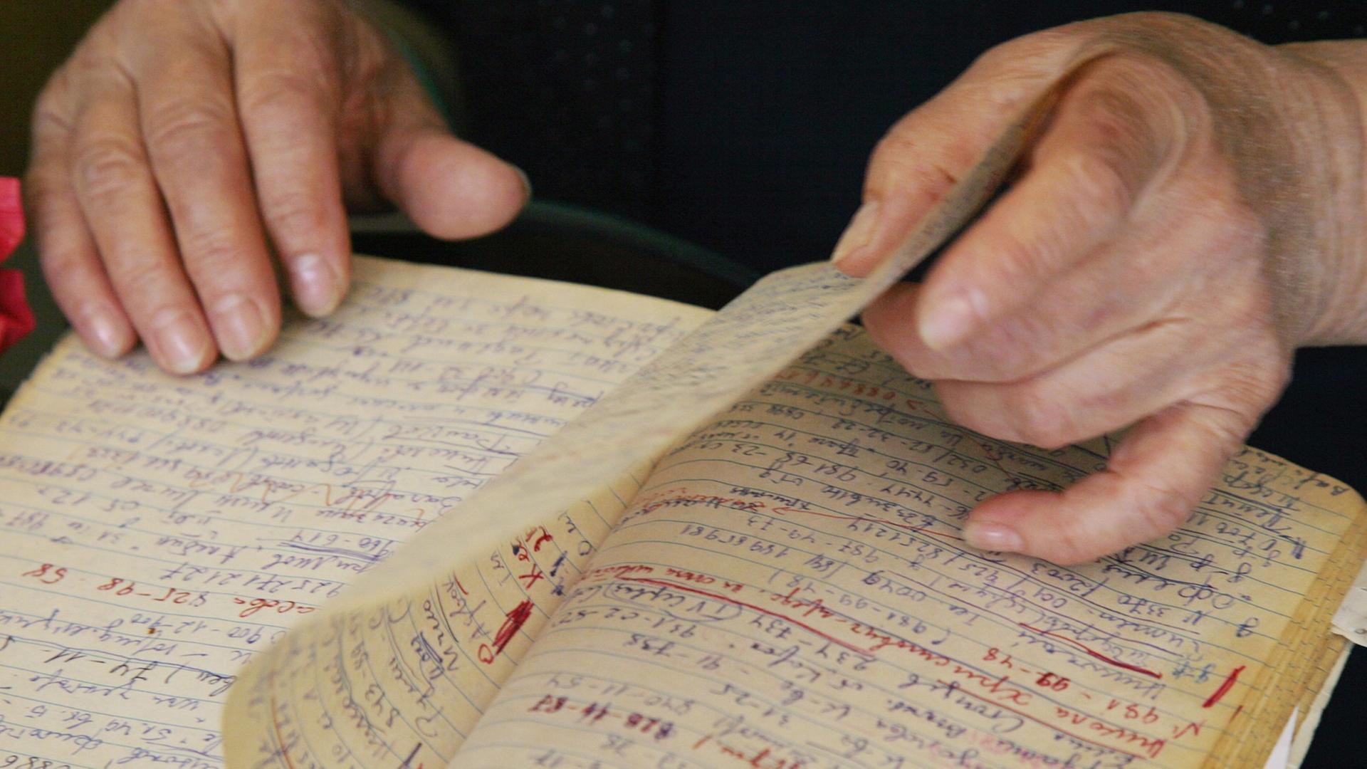 Eine ältere Frau blättert in einem Notizbuch - ihre Hände sind zu sehen.