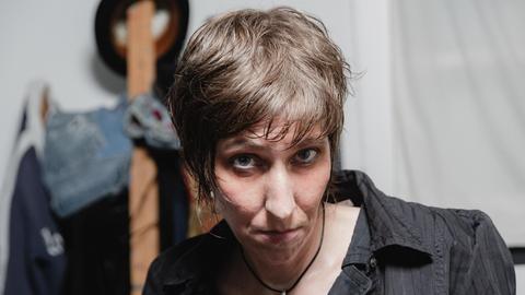 Eine Frau mit mittellangen, strähnigen dunkelblonden Haaren trägt ein dunkles Oberteil und blickt von unten in die Kamera.