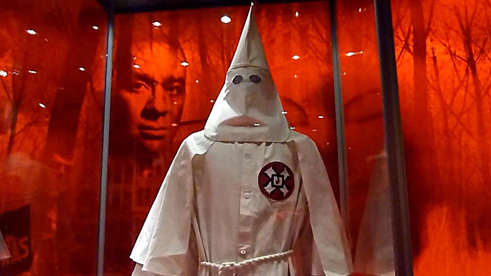 Die Robe eines Ku-Klux-Klan-Mitglieds, dahinter das Gesicht eines Schwarzen in einer Ausstellung in Washington.