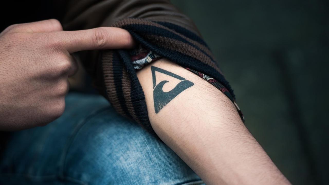 Ein Unterarm, auf dem ein Wellensymbol in einem Dreieck tätowiert ist.