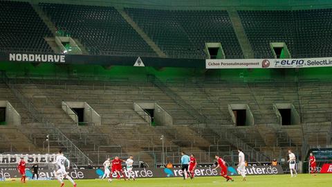 Borussia Mönchengladbach und der 1. FC Köln spielen im Borussia-Park vor leeren Zuschauerrängen. Im Vordergrund spielen sie Mannschaften gegeneinander. Im Hintergrund sind sie leeren Ränge zu sehen.