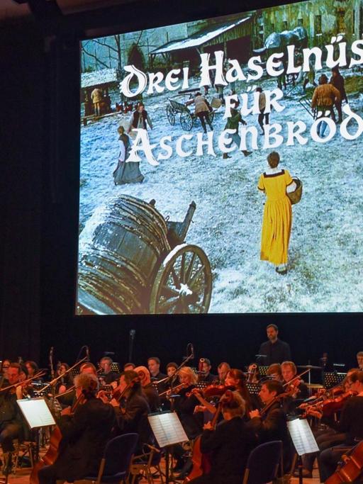 Auf eine Leinwand wird der Film "Drei Haselnüsse für Aschenbrödel" projiziert, davor sitzt ein Orchester und spielt die Filmmusik live.