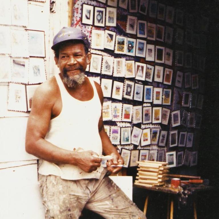 Frank Walter steht vor seinem Atelier (oder vielleicht auch Verkaufsraum) in Antigua, an der Wand hinter ihm hängen Dutzende seiner kleinen Arbeiten