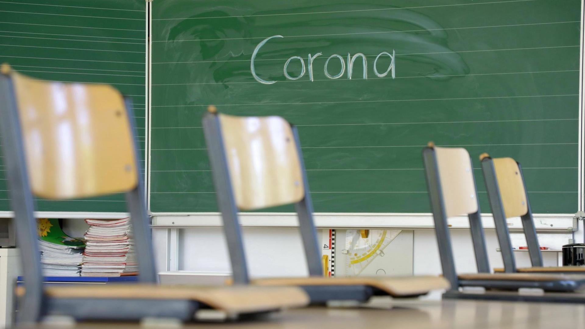 Stühle auf dem Tisch in einem Klassenzimmer. An der Tafel steht "Corona".