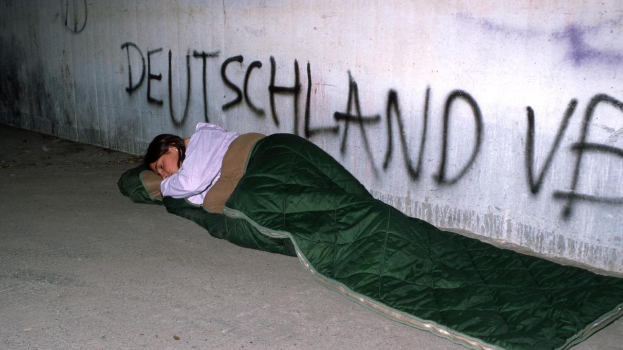 Eine junge Frau schläft in einem Schlafsack unter einer Brücke