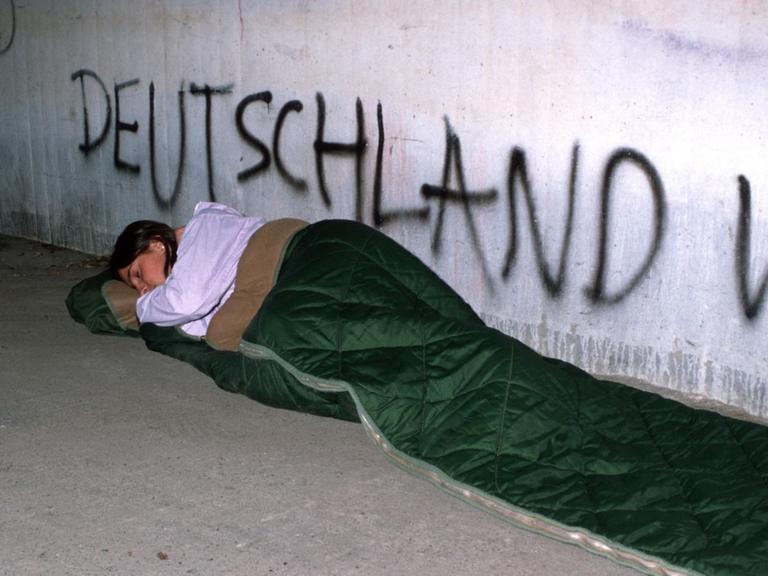Eine junge Frau schläft in einem Schlafsack unter einer Brücke