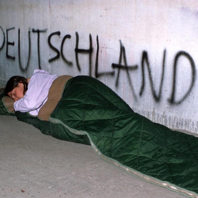 Eine junge Frau schläft in einem Schlafsack unter einer Brücke