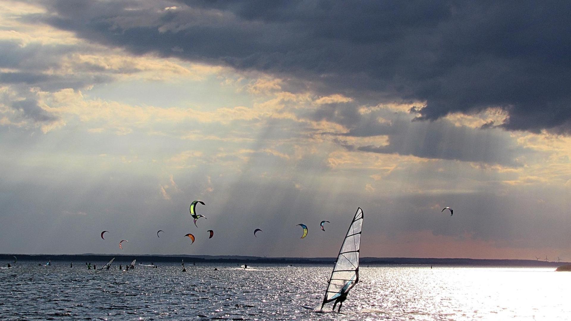 Mehrere Kitesurfer auf dem Meer, bei dramatischem Sonnenlicht.