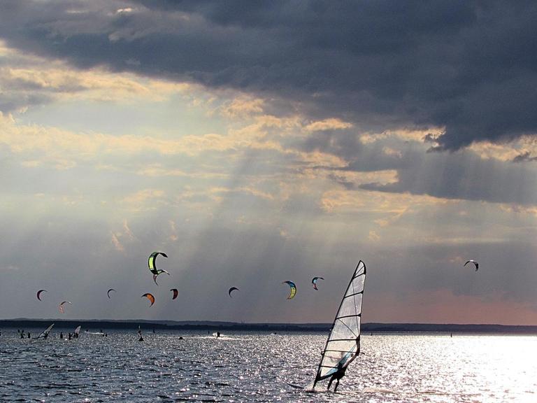 Mehrere Kitesurfer auf dem Meer, bei dramatischem Sonnenlicht.