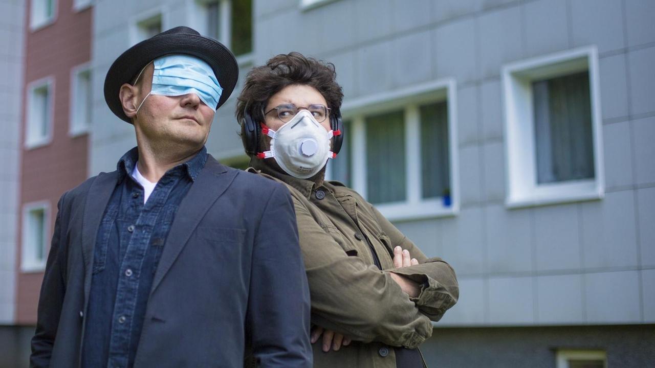 Devid Striesow und Axel Ranisch tragen Masken vor einem Plattenbau.