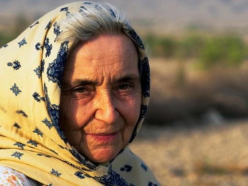 Ruth Pfau wird von der Sonne angestrahlt. Sie trägt ein gelb-blaues Tuch auf dem Kopf, das im Wind weht. Im Hintergrund ist Wüste.