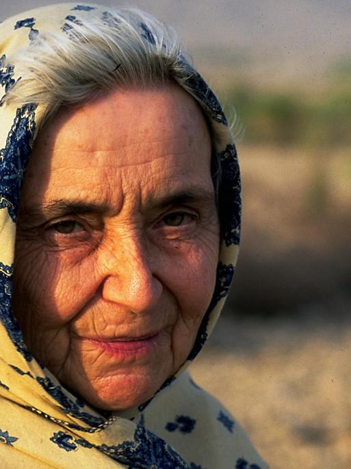 Ruth Pfau wird von der Sonne angestrahlt. Sie trägt ein gelb-blaues Tuch auf dem Kopf, das im Wind weht. Im Hintergrund ist Wüste.