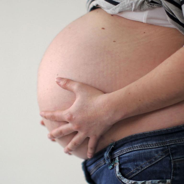 Eine schwangere Frau hält ihren Bauch.