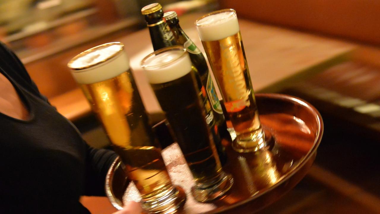 Eine Bedienung trägt am 29.10.2013 in Erfurt (Thüringen) in einem Lokal ein Tablett mit Bier. Der Mindestlohn gilt auch im Hotel- und Gaststättengewerbe.