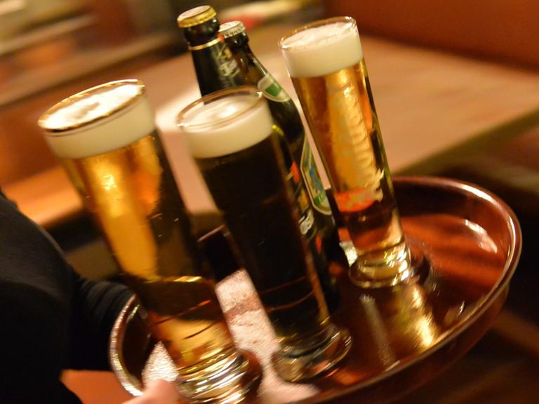 Eine Bedienung trägt am 29.10.2013 in Erfurt (Thüringen) in einem Lokal ein Tablett mit Bier. Der Mindestlohn gilt auch im Hotel- und Gaststättengewerbe.