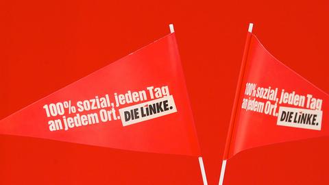 Zwei rote Fähnchen stehen vor rotem Hintergrund in einem Glas. Aufschrift: 100 Prozent sozial, jeden Tag, an jedem Ort. Die Linke.