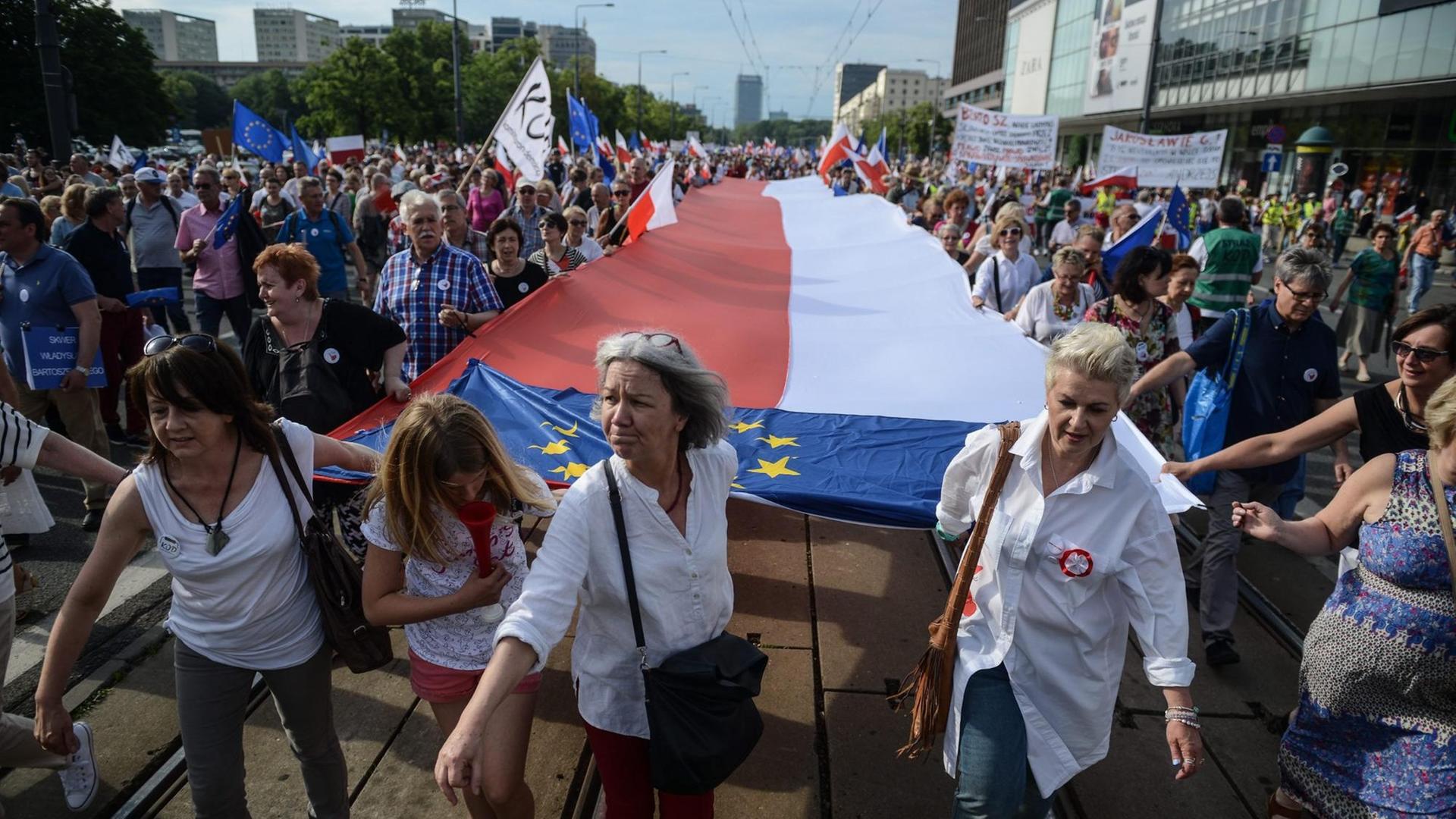 Bei einem regierungskritischen Protestmarsch der polnischen Opposition in Warschau ziehen Demonstranten eine große polnische und Europaflagge hinter sich her