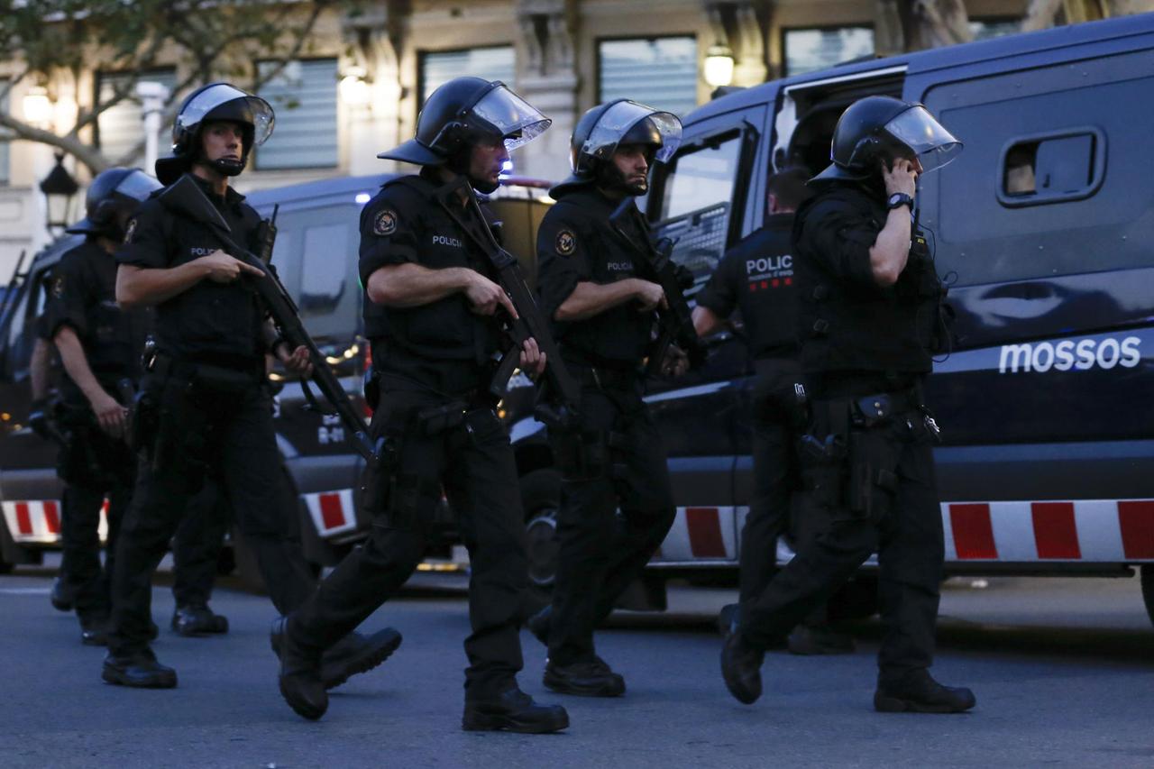 Mehrere Polizisten mit Helmen und Maschinepistolen rennen auf einer Straße an Polizeitransportern vorbei.