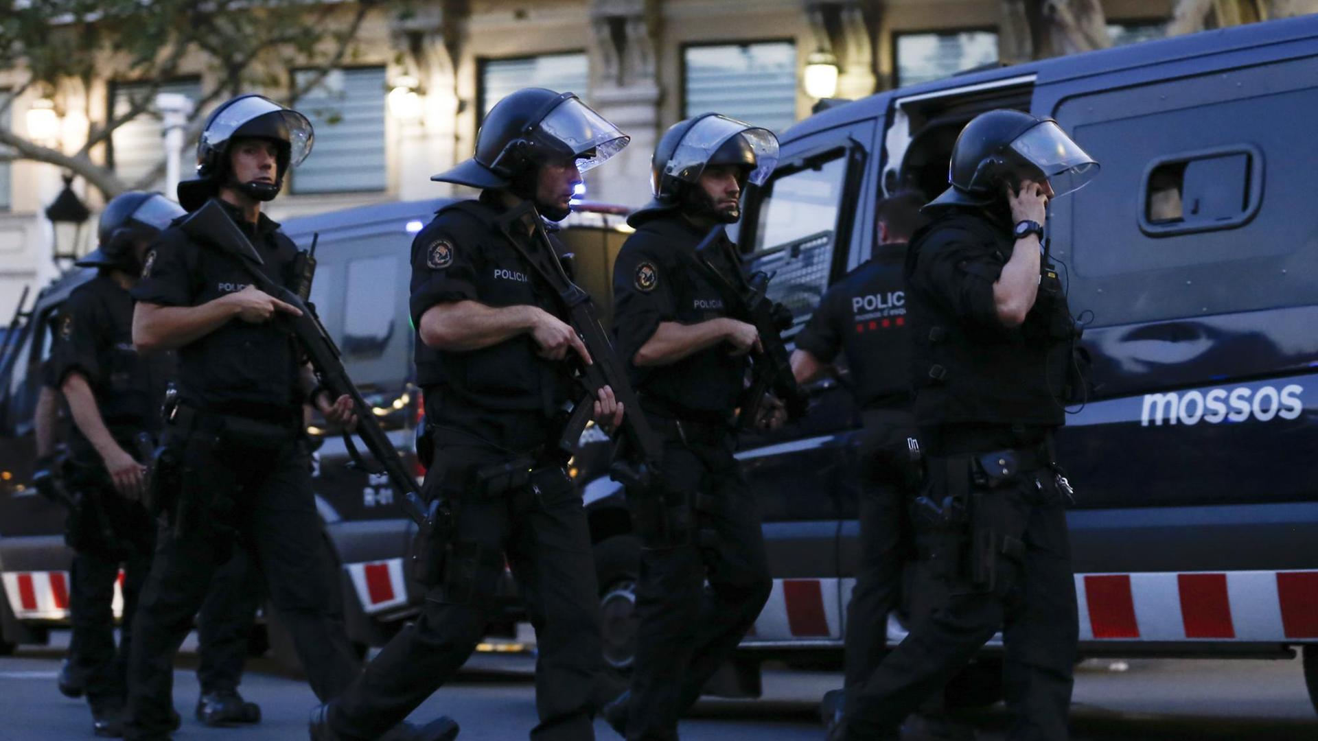 Mehrere Polizisten mit Helmen und Maschinepistolen rennen auf einer Straße an Polizeitransportern vorbei. Mehrere Polizisten mit Helmen und Maschinepistolen rennen auf einer Straße an Polizeitransportern vorbei.