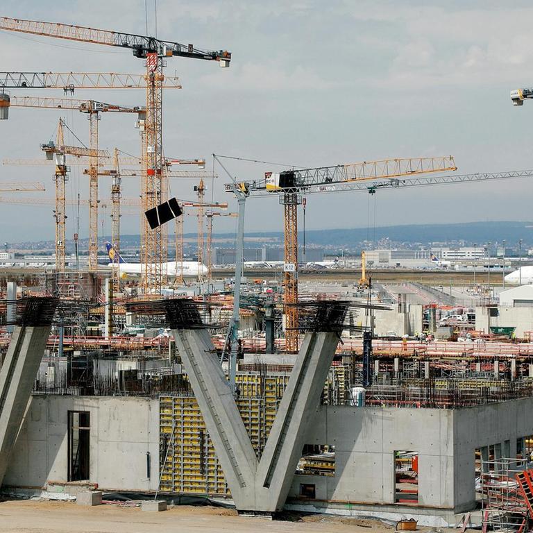 Kräne und Betronteile der Baustelle am Terminal 3. Im Hintergrund sind Flugzeuge zu sehen.