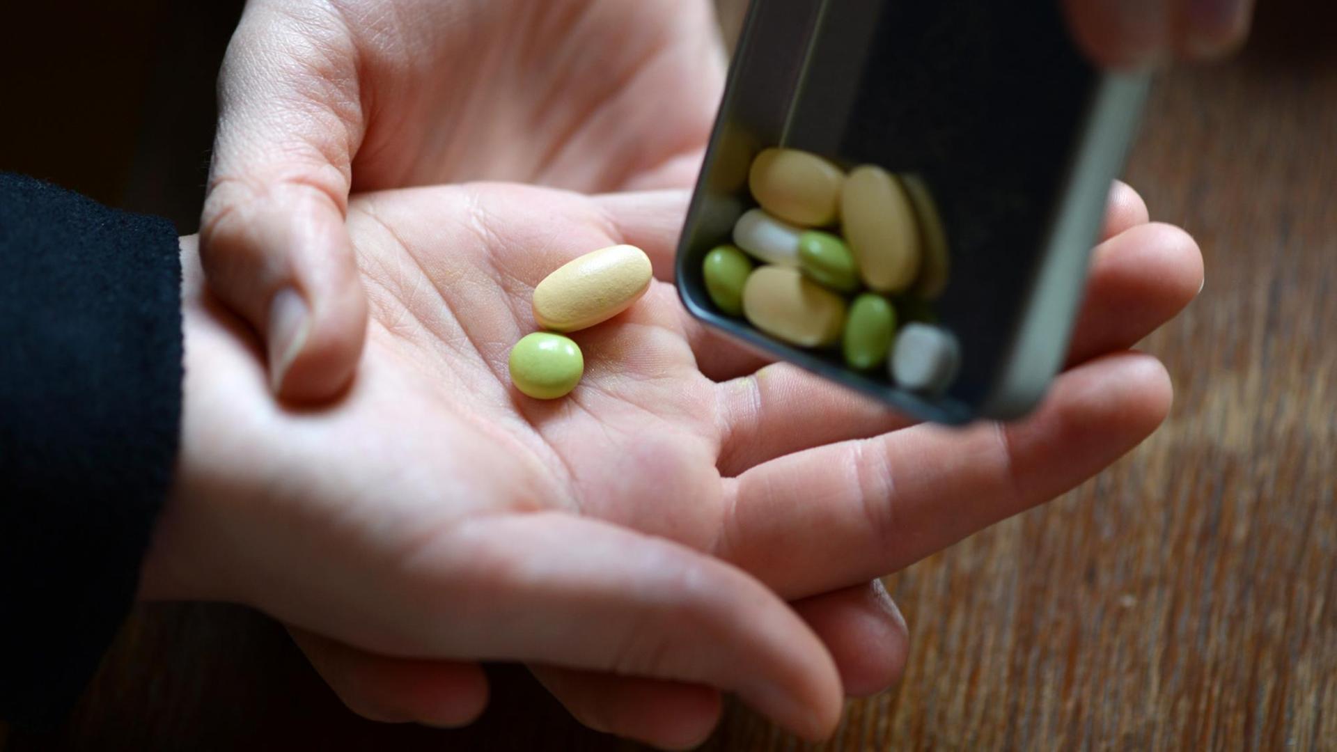 Ein Mädchen bekommt verschiedene Tabletten in die Hand geschüttet (Symbolbild)