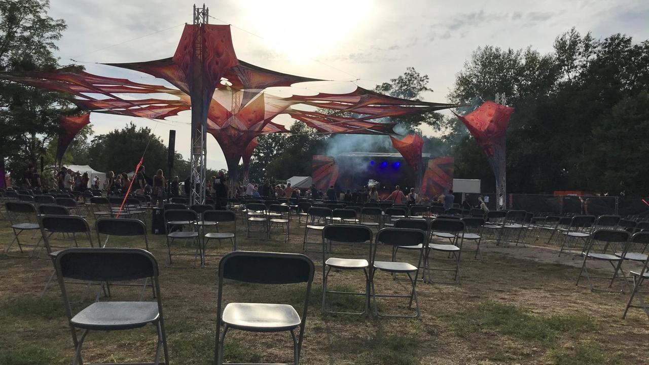 Das "Goa Nature"-Festival 2020, Blick auf Stuhreihen unter freiem Himmel, im Hintergrund Publikum und eine Bühne 