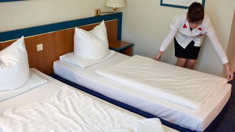 Eine Auszubildende zur Hotelfachfrau macht ein Bett in einem Zimmer in einem Hotel.