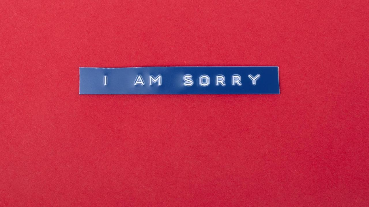 Auf rotem Untergrund liegt ein blauer Plastikstreifen auf den die Worte „I am sorry“ geprägt sind