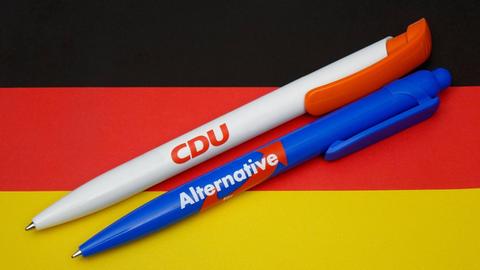 Kugelschreiber von CDU und AfD liegen auf einer Deutschlandfahne.