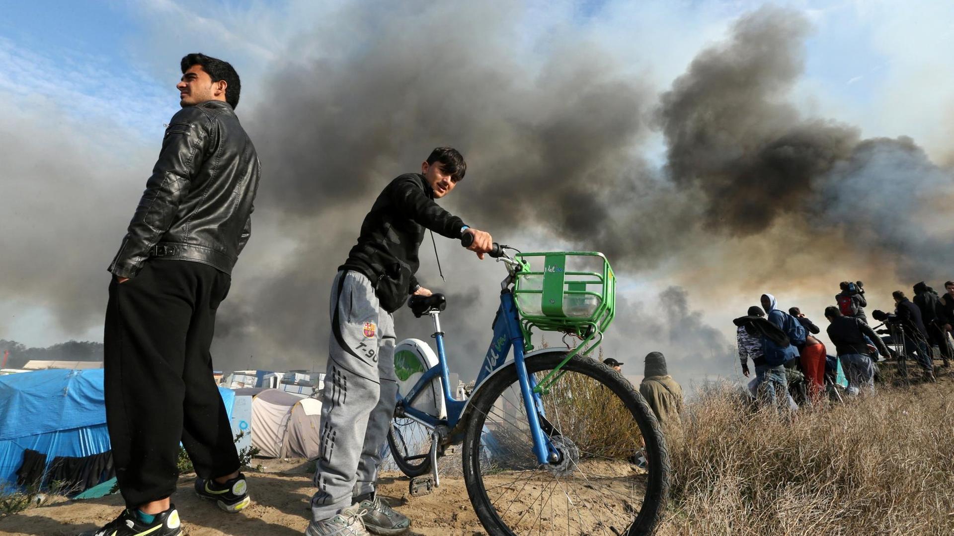 Flüchtlinge vor dem Camp in Calais während der Räumung, bei der zahlreiche Zelte und Hütten in Flammen aufgingen. 