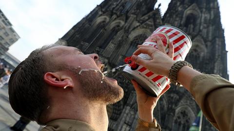Ein Karnevalist trinkt an Weiberfastnacht vor dem Dom Kölsch aus einem Fass.