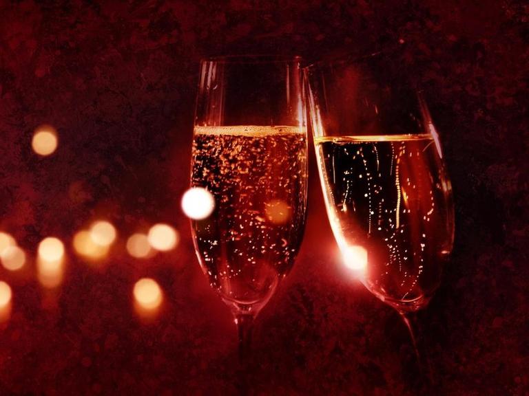 Zwei Champagnergläser vor einem festlichen roten Hintergrund, der in der Unschärfe liegt.