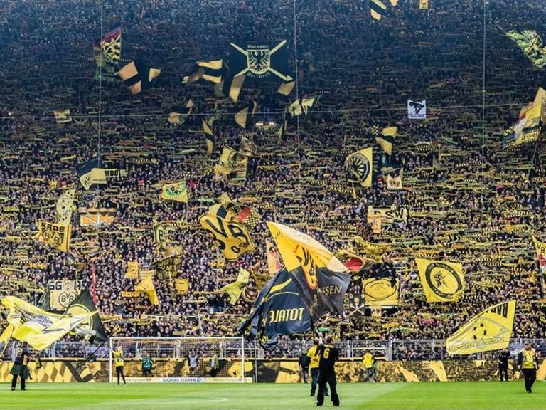 ARCHIV - Dicht gedrängt stehen Fans des Fußballclubs Borussia Dortmund am 27. April 2019 in der sogenannten Gelben Wand, der Südtribüne des Stadions schwenken gelbe Fahne und Schals.