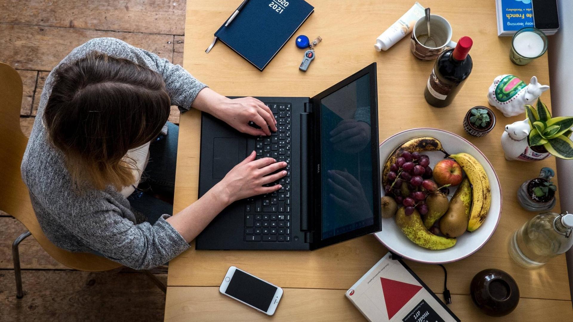 Eine Frau sitzt zu Hause an einem Tisch und arbeiten an ihrem Laptop