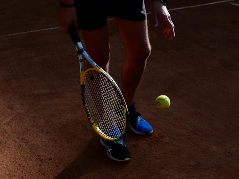 Ausschnitt eines Tennisspielers mit Schläger und Ball, der vom Sonnenlicht gestriffen wird.