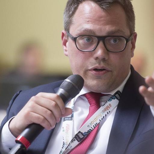 Wölken im Podiumsgespräch, gestikuliert mit einer Hand und hält mit der anderen ein Mikro.