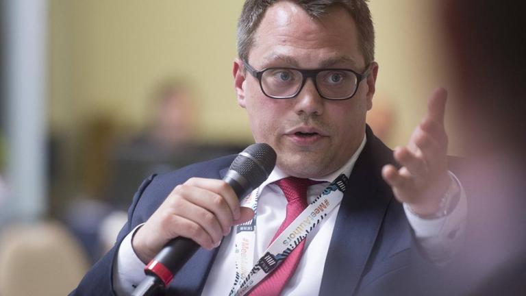 Wölken im Podiumsgespräch, gestikuliert mit einer Hand und hält mit der anderen ein Mikro.