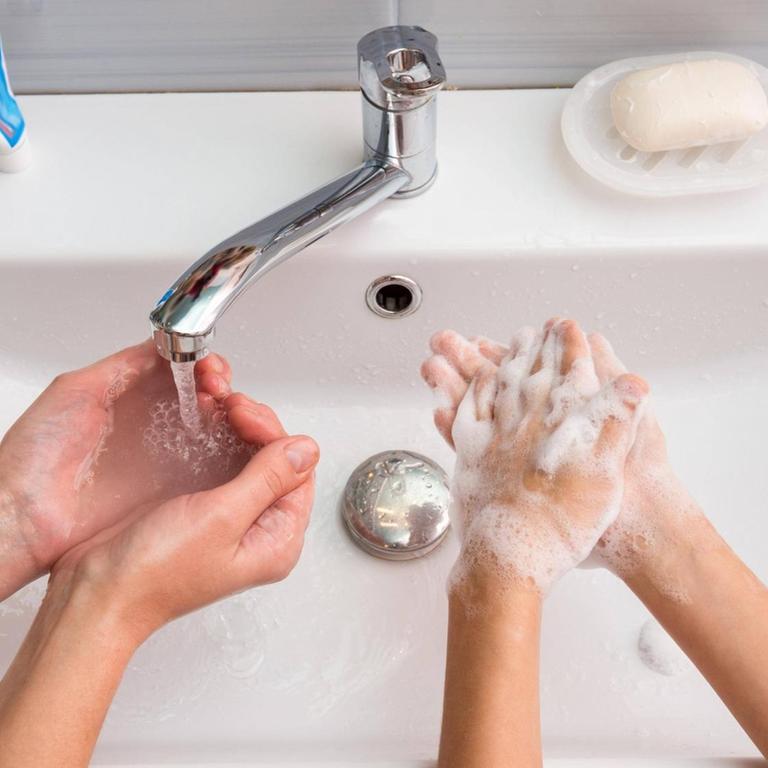 Ein Erwachsener und ein Kind waschen sich zuhause am Waschbecken die Hände.