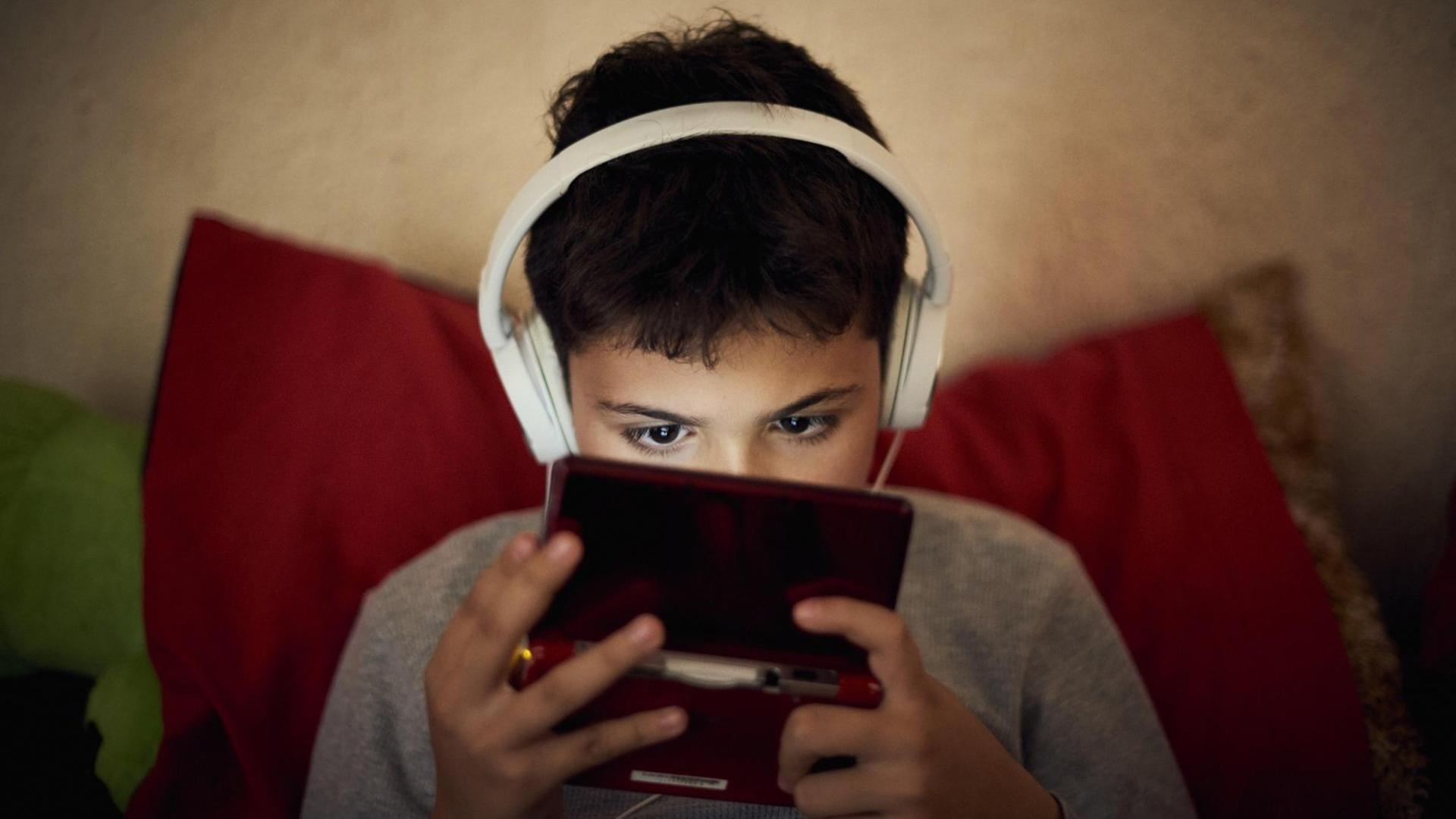 Symbolbild: Kind schaut in Handy, Kopfhörer auf den Ohren