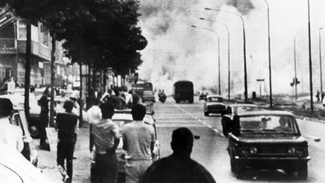 Straßenkampf zwischen vor allem Jugendlichen aus den ärmeren Stadtvierteln und der Polizei am 03.07.1969 in Turin. Auf einer Straße sind Demonstranten und fahrende Autos zu sehen, im Hintergrund Tränengaswolken.